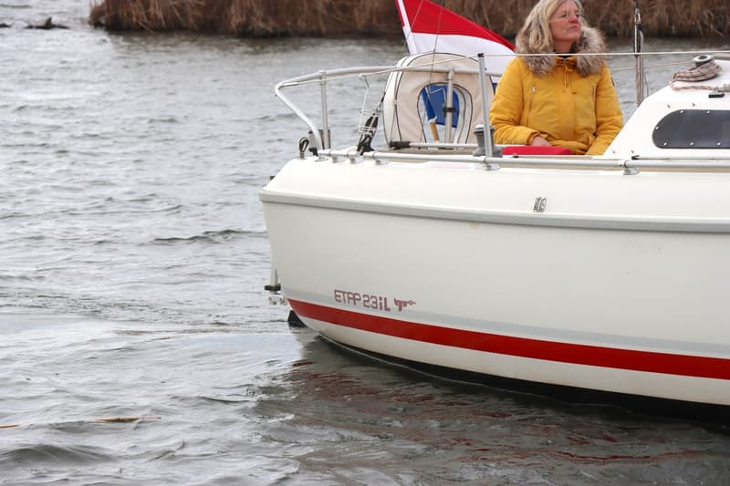 Een witte boot met rode streep en de tekst "ETAP 23iL" vaart op water met een vrouw in gele jas aan boord. — Etap 23 iL