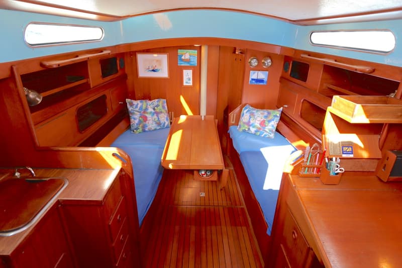 De foto toont het interieur van een boot met twee bedden, een tafel, houten meubels en een kleine gootsteen. — Koopmans 36