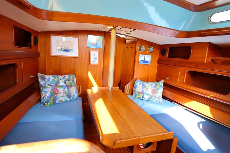 De foto toont het interieur van een boot met houten wanden, twee blauwe banken met kussens en een houten tafel. — Koopmans 36