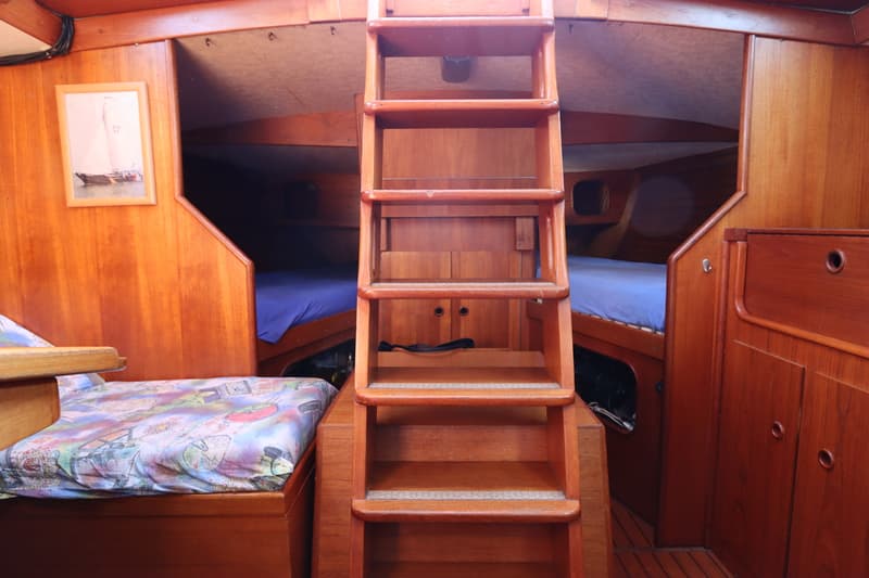 De foto toont het interieur van een boot met houten wanden, een trap in het midden en twee bedden met blauwe lakens.