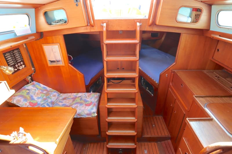 De foto toont het interieur van een boot met houten afwerking, een trap, twee bedden en een kombuis. — Koopmans 36