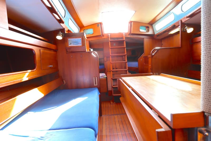 De foto toont het interieur van een boot met houten wanden, vloer en meubilair, blauwe matrassen en een ladder. — Koopmans 36