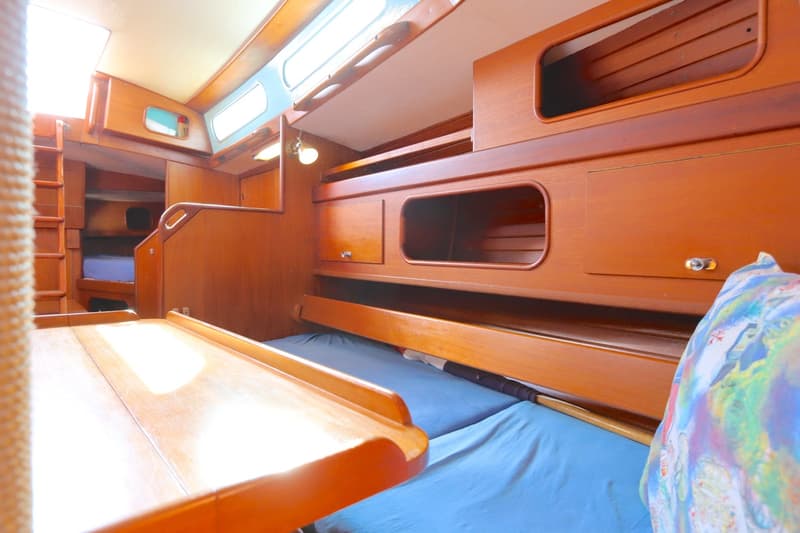 De foto toont een houten interieur van een boot met een tafel, bedden met blauwe lakens en opbergruimte. — Koopmans 36
