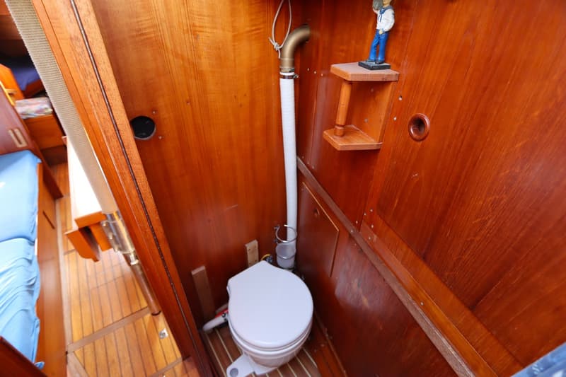 Een toiletruimte met houten wanden en vloer, een wit toilet en een afvoerbuis.