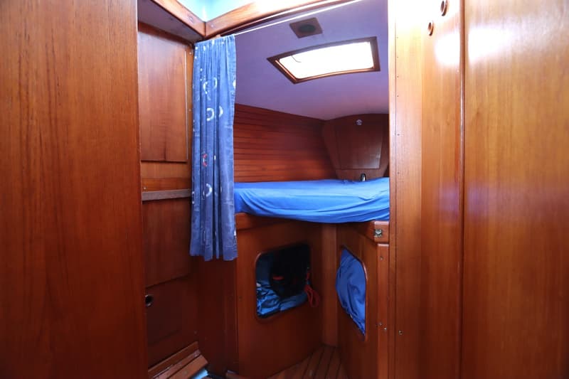 Een kajuit met een bed met blauw laken, een blauw gordijn en een dakraam. — Koopmans 36