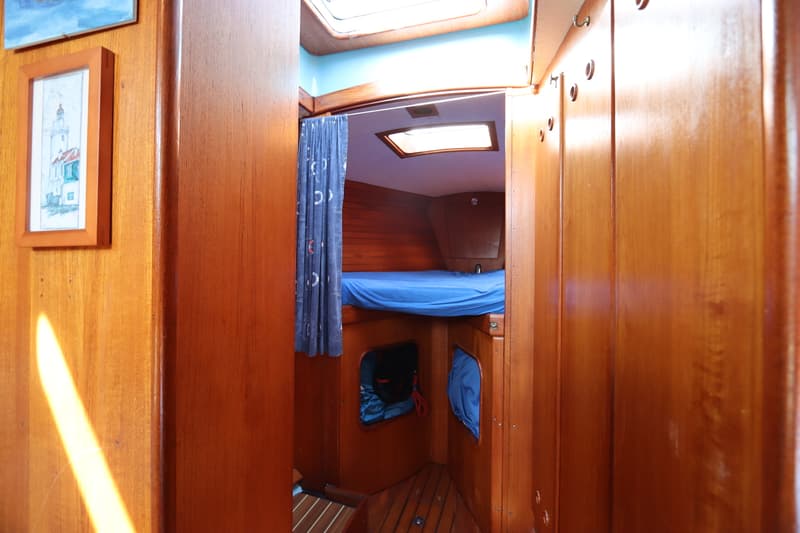 De foto toont een houten interieur van een boot met een blauw opgemaakt bed, een gordijn en een ingelijste tekening.