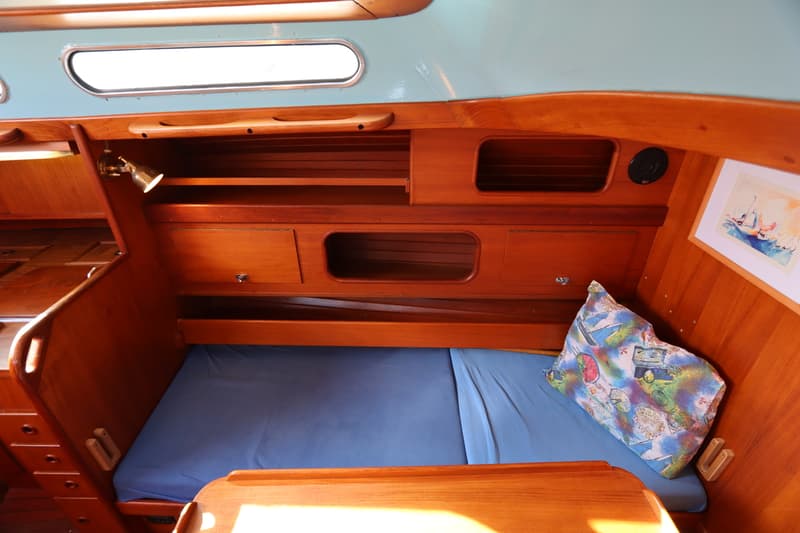 De foto toont een kajuit met houten interieur, een blauw bed, een kussen en een ingelijste afbeelding. — Koopmans 36
