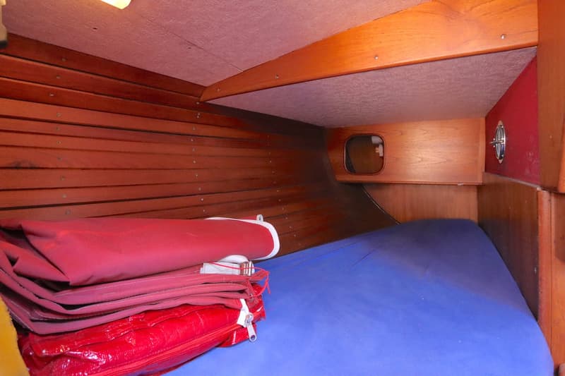 De foto toont een kajuit met houten lambrisering, een blauw matras en opgevouwen rode zeilen. — Koopmans 36
