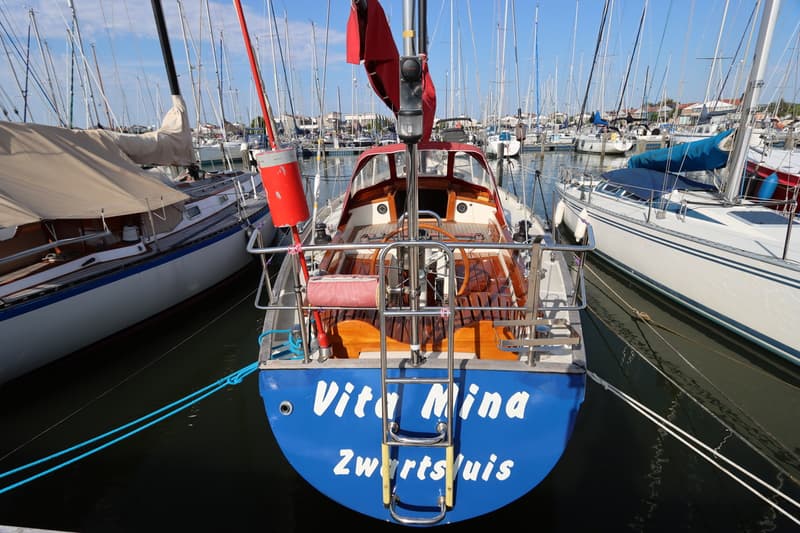 Een blauwe zeilboot met de naam "Vita Mina Zwartsluis" ligt aangemeerd in een haven vol met andere zeilboten. — Koopmans 36