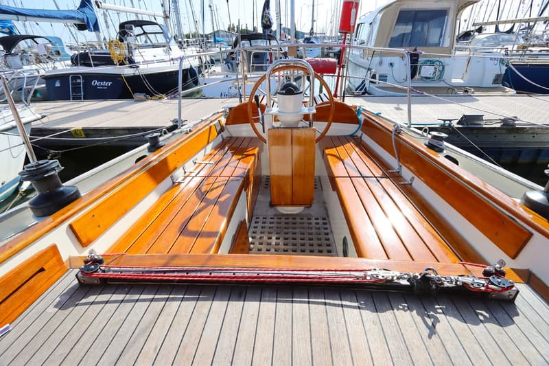 De foto toont de kuip van een zeilboot met een houten stuurwiel en banken, en een teakdek. — Koopmans 36