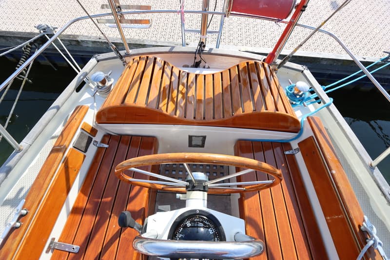 Een bovenaanzicht van de kuip van een zeilboot met een houten stuurwiel, kompas en houten banken. — Koopmans 36