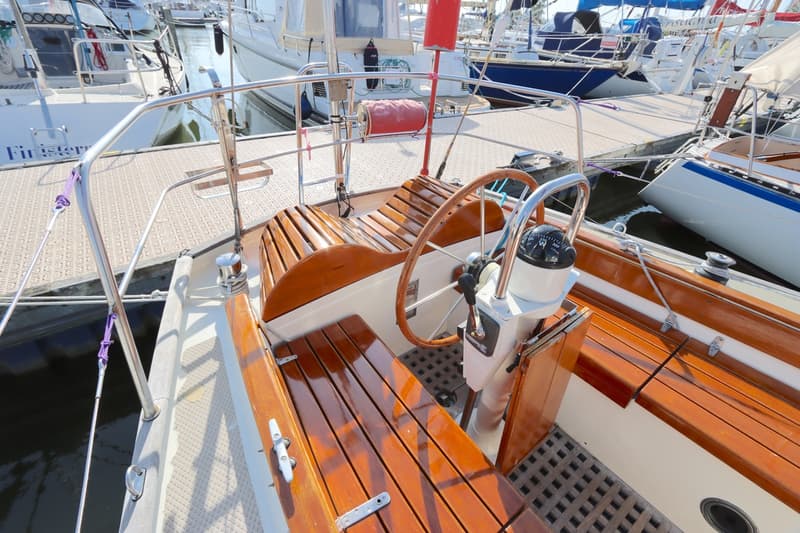 Een houten stuurwiel en kompas zijn zichtbaar in de kuip van een zeilboot, omringd door houten banken. — Koopmans 36