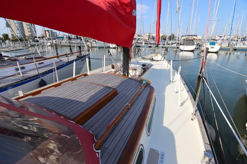 Een rode zeilhoes bedekt een deel van het zeil van een boot met een houten dek, liggend in een jachthaven. — Koopmans 36