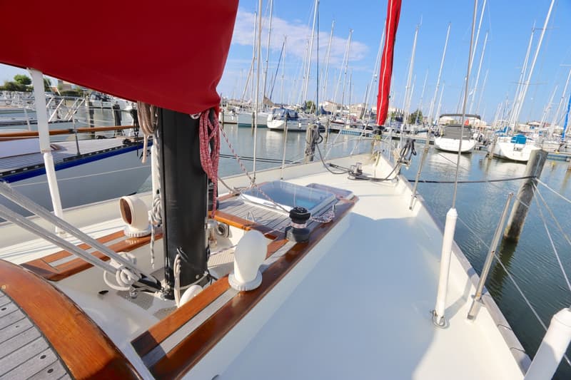 Een dek van een zeilboot met een rode zeilhoes, omringd door andere zeilboten in een haven. — Koopmans 36