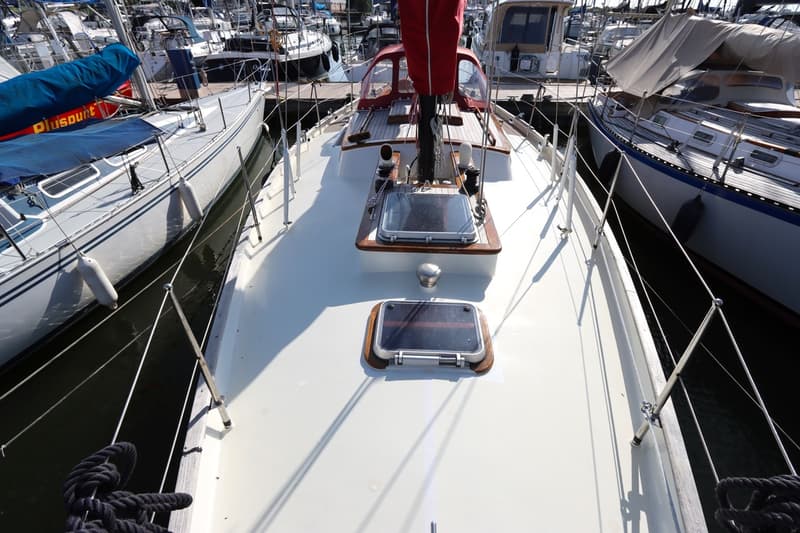 Een bovenaanzicht van het dek van een witte zeilboot met twee luiken en een rode zeilhoes, omringd door andere boten in een…