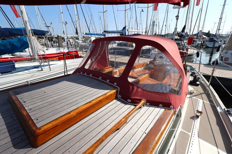 Een zeilboot met een rood buiskap en een houten dek ligt in een haven vol met andere zeilboten. — Koopmans 36