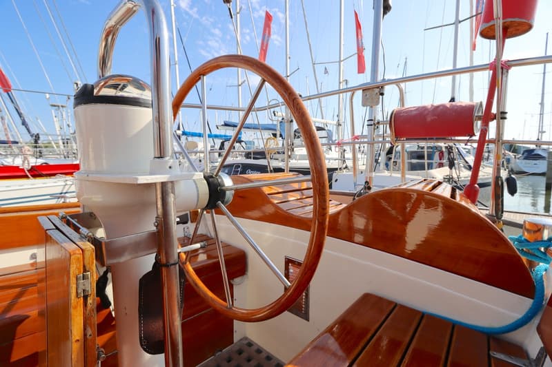Een houten stuurwiel en een kompas op een zeilboot, met andere boten op de achtergrond. — Koopmans 36
