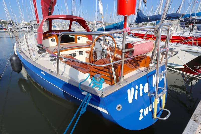 Een blauwe zeilboot met een rode buiskap en houten details ligt aangemeerd in een haven. — Koopmans 36