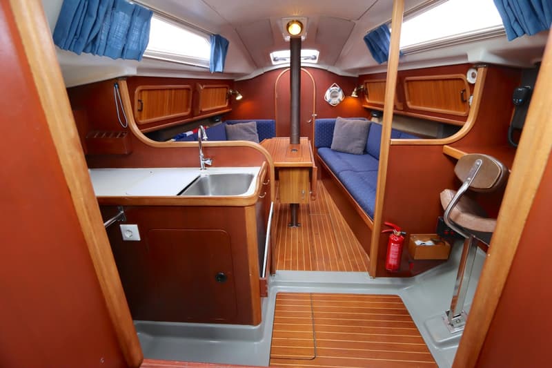 Een interieur van een boot met houten vloer, blauwe banken, een keukenblok met spoelbak en een tafel. — Dehler 34 Optima 106