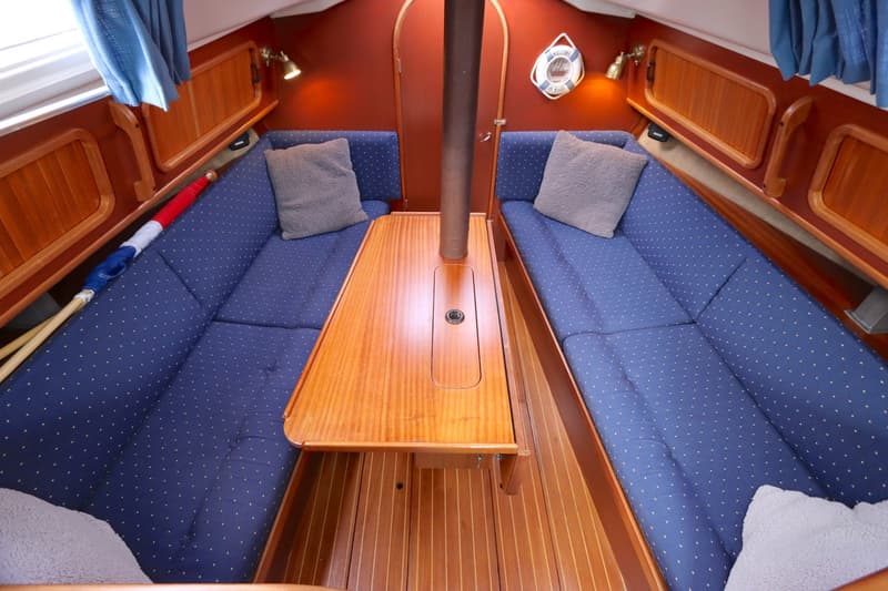 De foto toont het interieur van een boot met twee blauwe banken, een houten tafel en een houten vloer. — Dehler 34 Optima 106