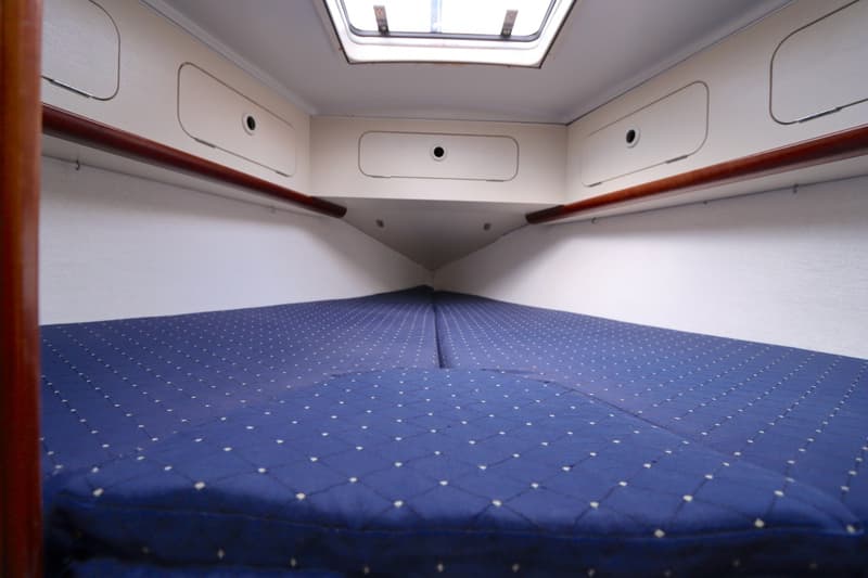 De foto toont een kajuit met een blauw matras met witte stippen, opbergvakken en een dakraam. — Dehler 34 Optima 106