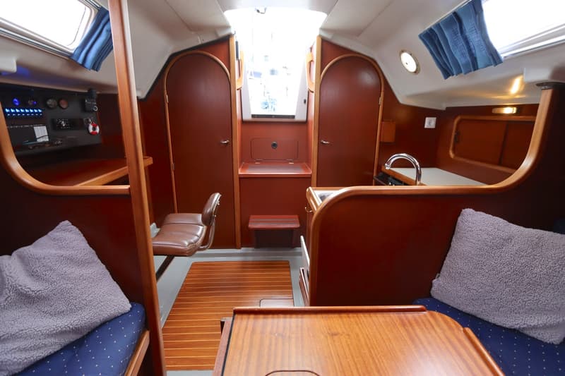 De foto toont het interieur van een boot met houten panelen, een kombuis, een navigatiehoek en slaapplaatsen.