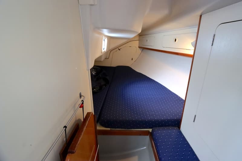 De foto toont een kajuit met een groot blauw gestippeld bed en een kleiner bijpassend zitkussen. — Dehler 34 Optima 106
