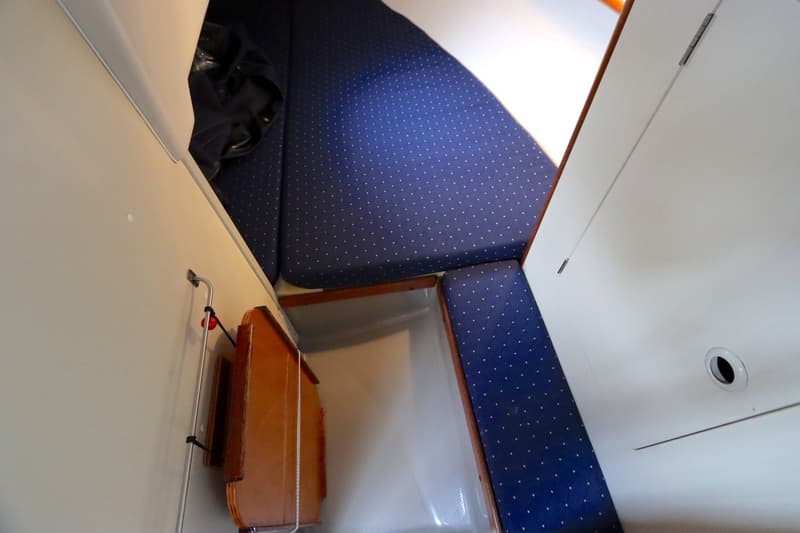 De foto toont een interieur van een boot met blauwe gestippelde kussens, witte wanden en een houten kastje.