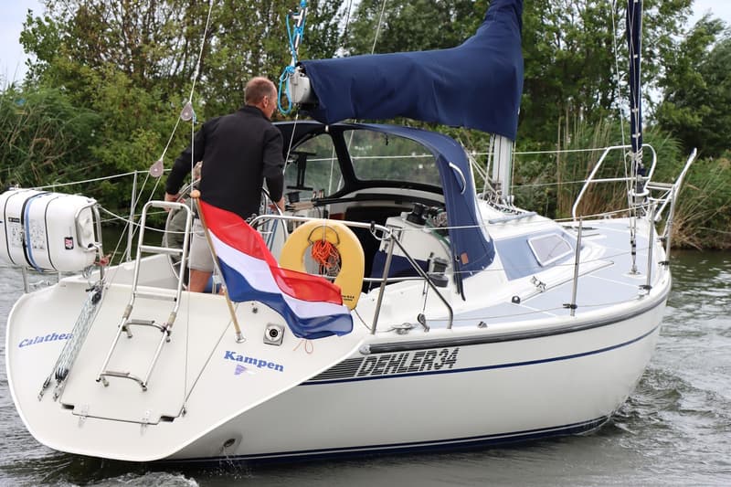 Een witte zeilboot met blauwe accenten en de naam "DEHLER 34" op de romp vaart op het water. — Dehler 34 Optima 106