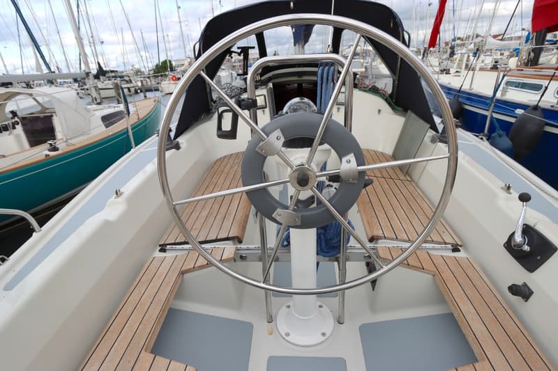 Een stuurwiel met grijze handgreep en houten banken op een boot, met andere boten op de achtergrond. — Dehler 34 Optima 106