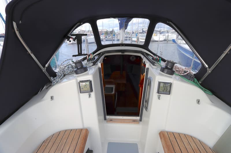 Een bovenaanzicht van de kuip van een zeilboot met een donkerblauwe buiskap en uitzicht op de haven. — Dehler 34 Optima 106