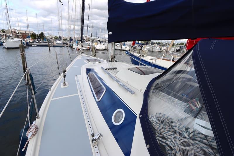 Een zeilboot met een blauw dekzeil en een blauwe streep op de romp ligt in een jachthaven. — Dehler 34 Optima 106