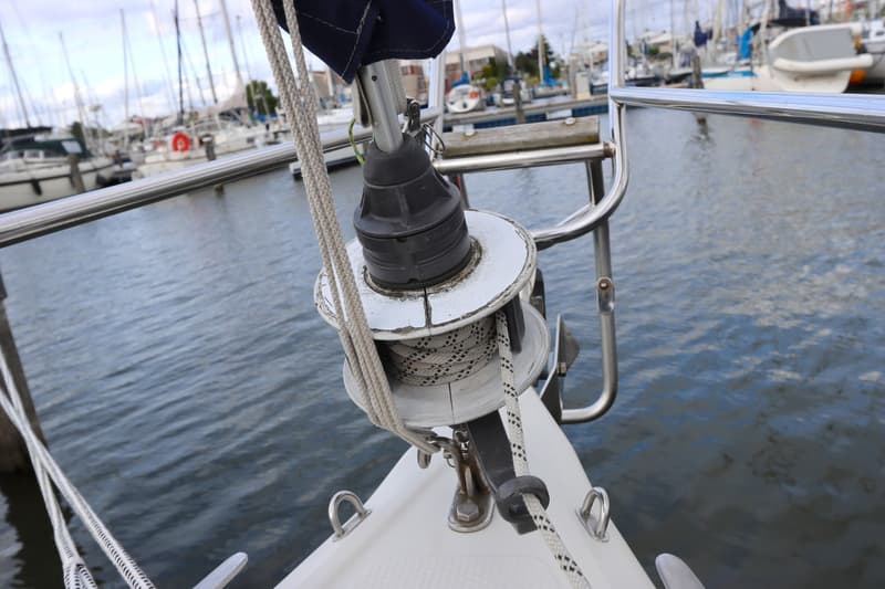 Een detailfoto van de voorstagrol van een zeilboot, met touw eromheen gewikkeld, en water op de achtergrond.