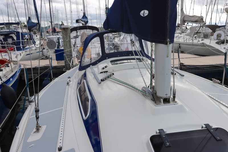 Een witte zeilboot met blauwe accenten en een blauwe buiskap ligt in een haven vol met andere zeilboten.