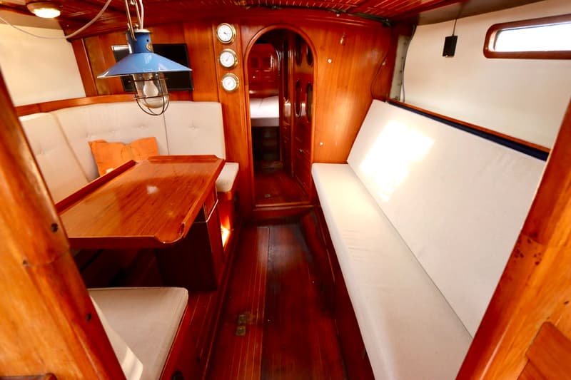 De foto toont het interieur van een boot met houten wanden en vloer, witte banken en een houten tafel. — RJ 140