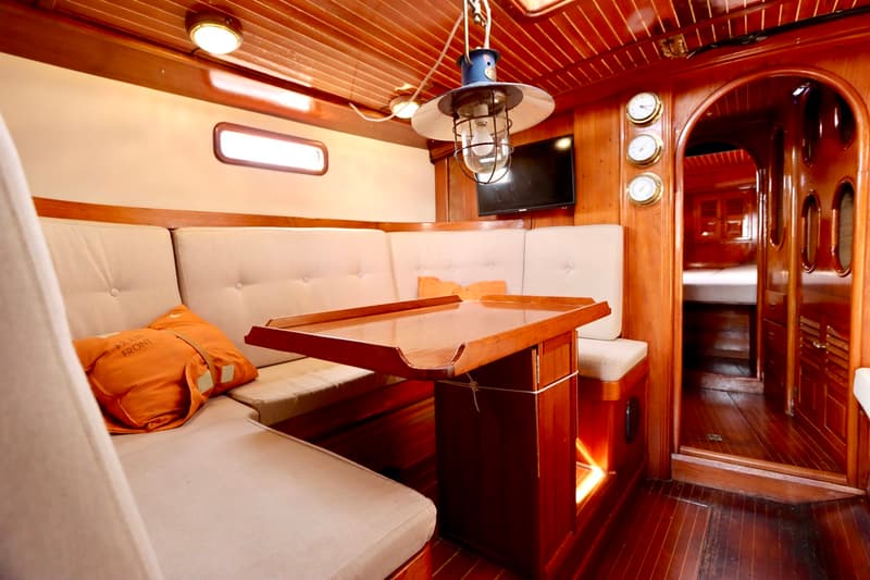 De foto toont het interieur van een boot met houten wanden en plafond, een zithoek met lichte kussens en een houten tafel.