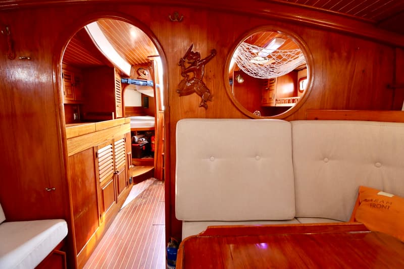 De foto toont het interieur van een boot met veel houtwerk, een bank met lichte kussens en een ronde spiegel. — RJ 140