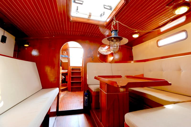 De foto toont het interieur van een boot met houten wanden en plafond, witte kussens en een houten tafel. — RJ 140