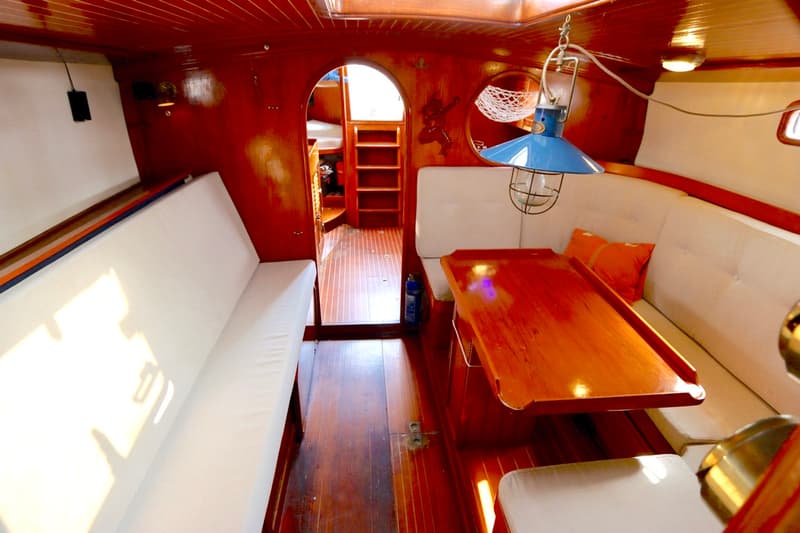 De foto toont het interieur van een boot met houten wanden en vloer, witte banken en een houten tafel. — RJ 140