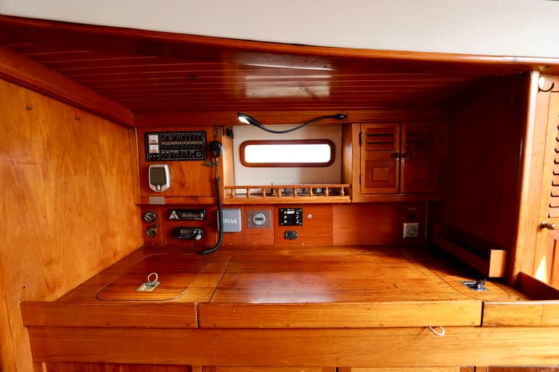 Een houten interieur van een boot met een werkblad, diverse meters, schakelaars en een klein raam. — RJ 140