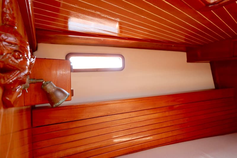 De foto toont een interieur van een boot met houten lambrisering en een klein raam. — RJ 140