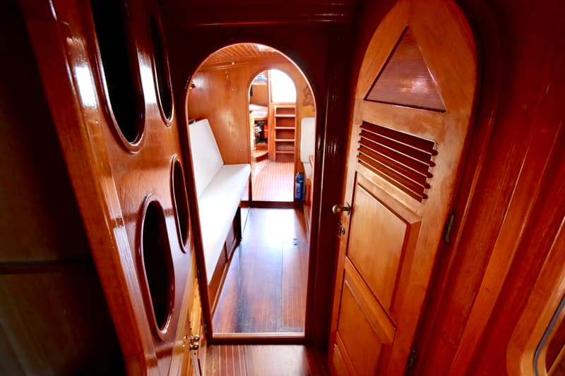Een houten interieur van een boot met een gang, zitbanken, een deur en een brandblusser. — RJ 140