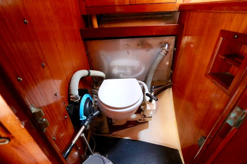 Een scheepstoilet met een handpomp en houten lambrisering in een kleine ruimte.