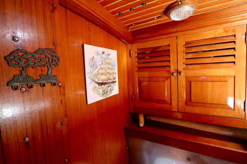 De foto toont een interieur met houten lambrisering, een kapstok, een tegel met een zeilschip en een houten kast met…