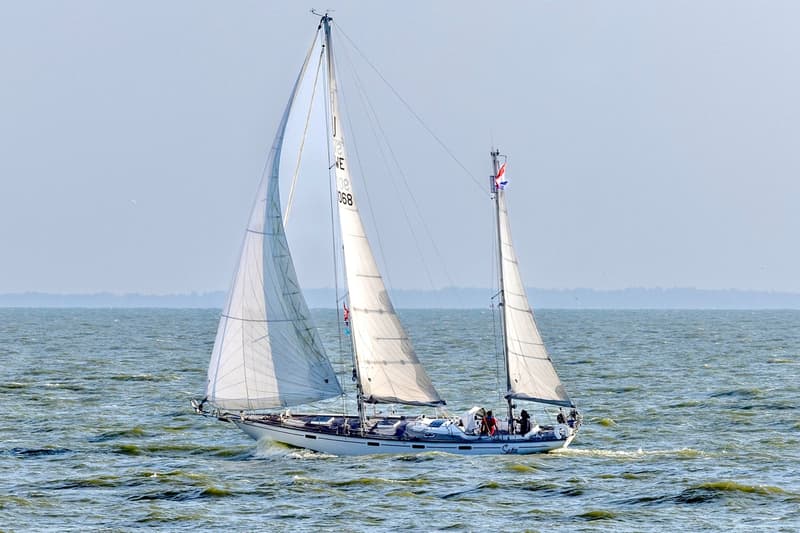 Een witte zeilboot met twee masten en witte zeilen vaart op een waterlichaam met golven. — RJ 140