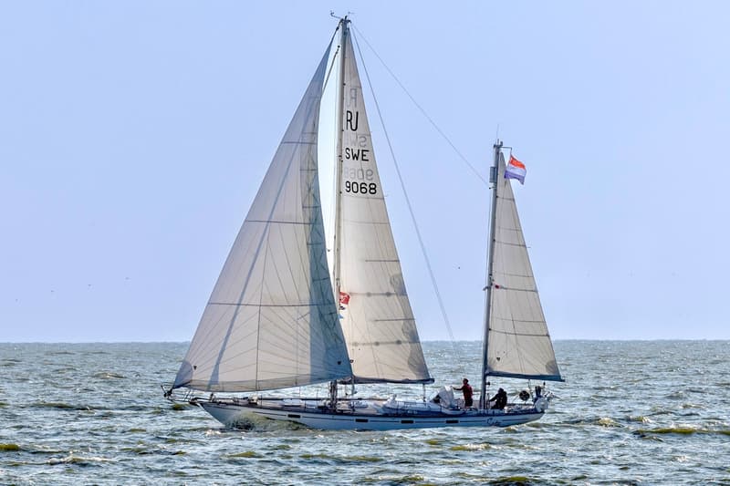 Een zeilboot met twee masten en witte zeilen vaart op een licht golvende zee onder een heldere hemel. — RJ 140
