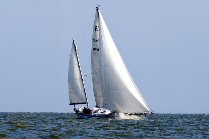 Een zeilboot met twee masten en witte zeilen vaart op een golvende zee onder een heldere hemel. — RJ 140