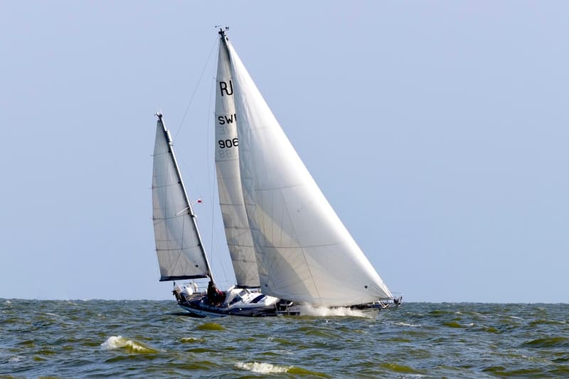 Een zeilboot met twee witte zeilen en de letters "RJ SWI 906" op het voorste zeil vaart op golvend water. — RJ 140