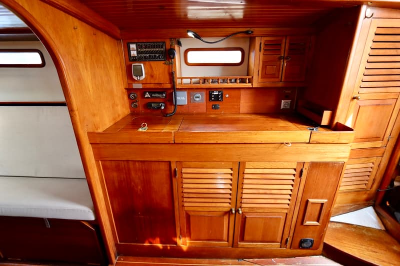 Een houten interieur van een boot met een bankje, een werkblad, diverse instrumenten en opbergkasten. — RJ 140