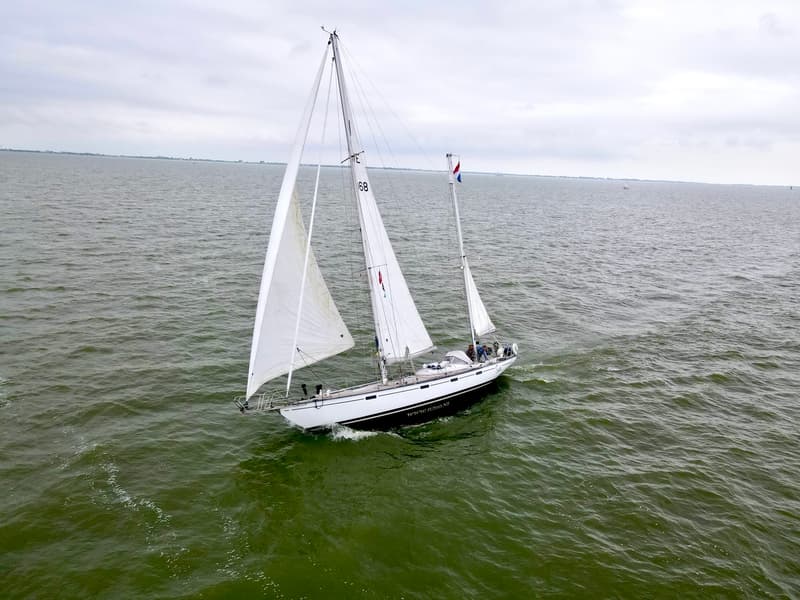 Een witte zeilboot met zwarte streep vaart op een grijsgroene zee onder een bewolkte hemel. — RJ 140